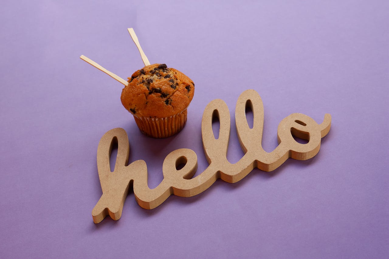 Close-up of a cupcake with 'hello' sign on a purple surface, perfect for greeting cards.